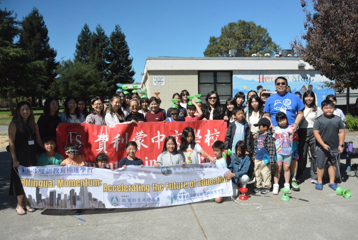FCS students, teachers, and the visiting Taiwan delegation posing together outdoors with a Fremont Chinese School banner and diabolos.