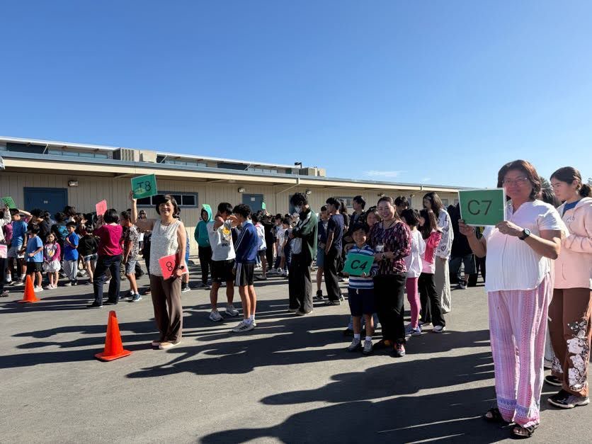 Students and teachers gathered outside holding classroom number signs after the fire drill.